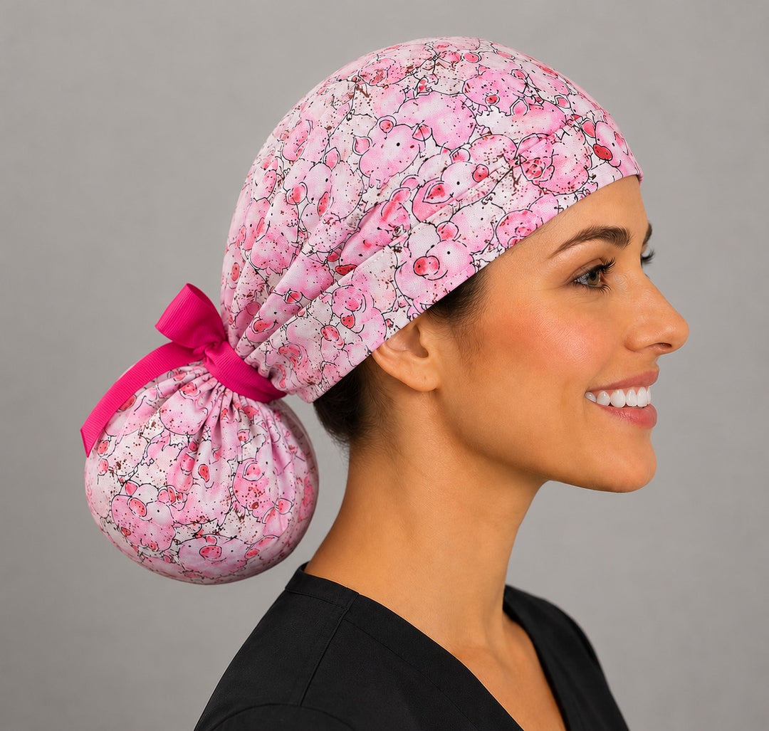 Woman wearing pink pig ponytail scrub cap, front view smiling with all-over cute cartoon pigs print and hot pink ribbon tie