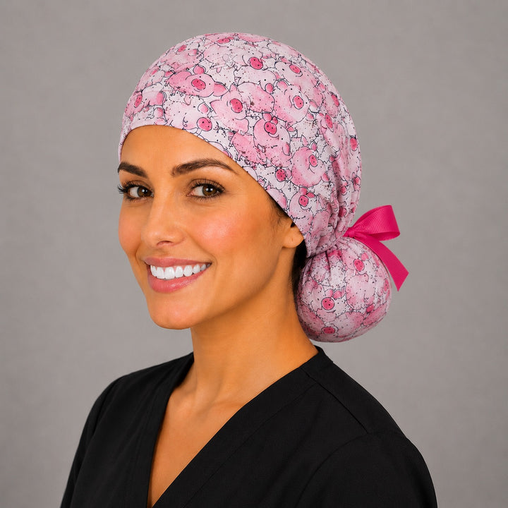 Pink pig ponytail nurse cap right three-quarter angle on smiling model showing cartoon pigs print and hot pink grosgrain ribbon bow