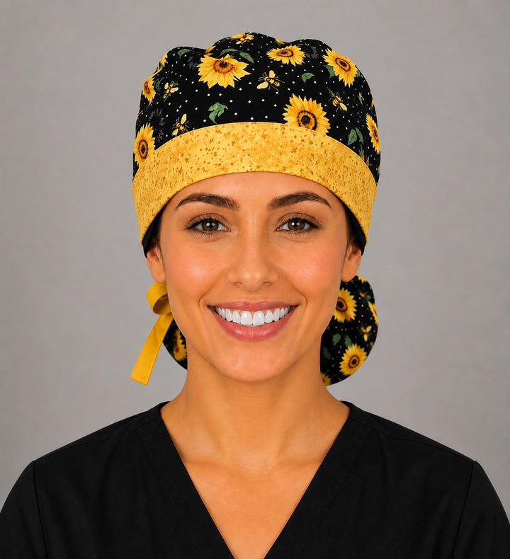 Woman wearing sunflower and bee ponytail scrub cap, front view smiling with golden sunflowers, honey bees on black and gold speckled band