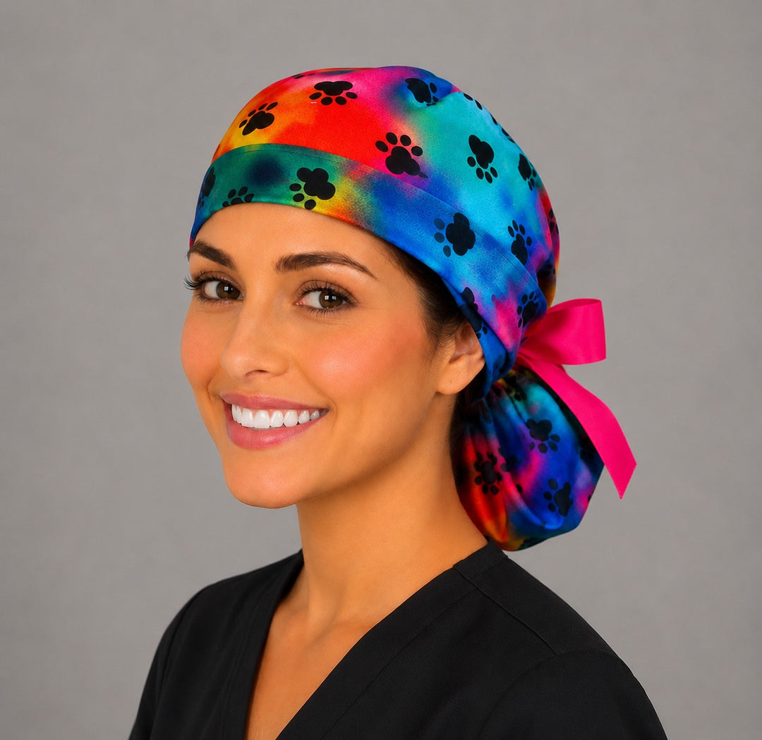 Tie dye puppy paw rainbow ponytail nurse cap right three-quarter angle on smiling model showing black paw prints and pink bow