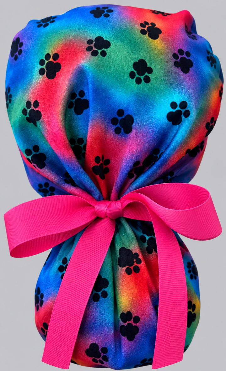 Tie dye puppy paw rainbow ponytail scrub cap back view showing double gathered pouch of black paw prints and hot pink ribbon bow