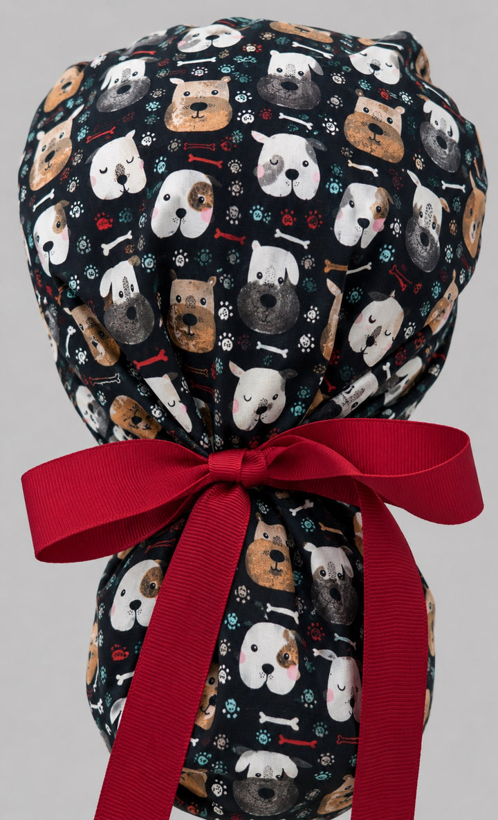 Woman wearing puppy dog lover ponytail scrub cap, front view smiling with cartoon dog faces, bones, paw prints on black and red ribbon tie