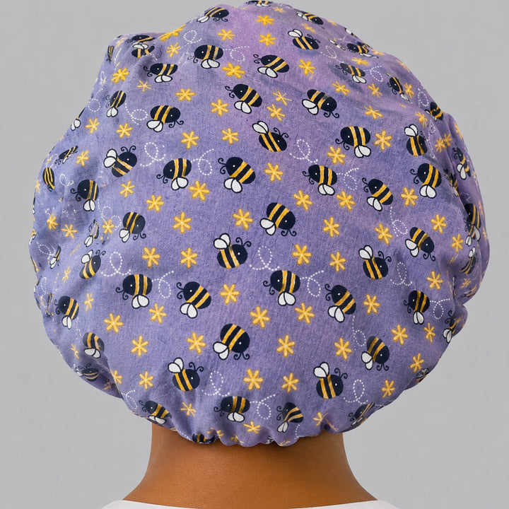 Back view of the purple bee bouffant scrub cap showing the full roomy fit and elastic gathered back — lavender bumblebee and flower print