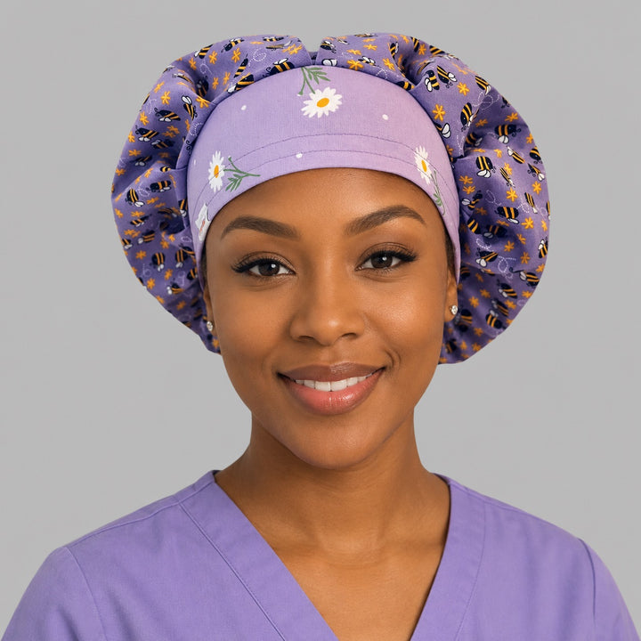 Woman wearing a purple bee and daisy bouffant scrub cap, front view — lavender bumblebee floral print with white daisy band, adjustable women&