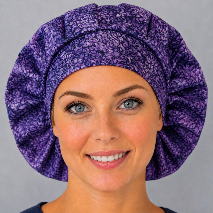 Woman wearing a purple floral bouffant scrub cap, front view — layered violet chrysanthemum petals, adjustable women&