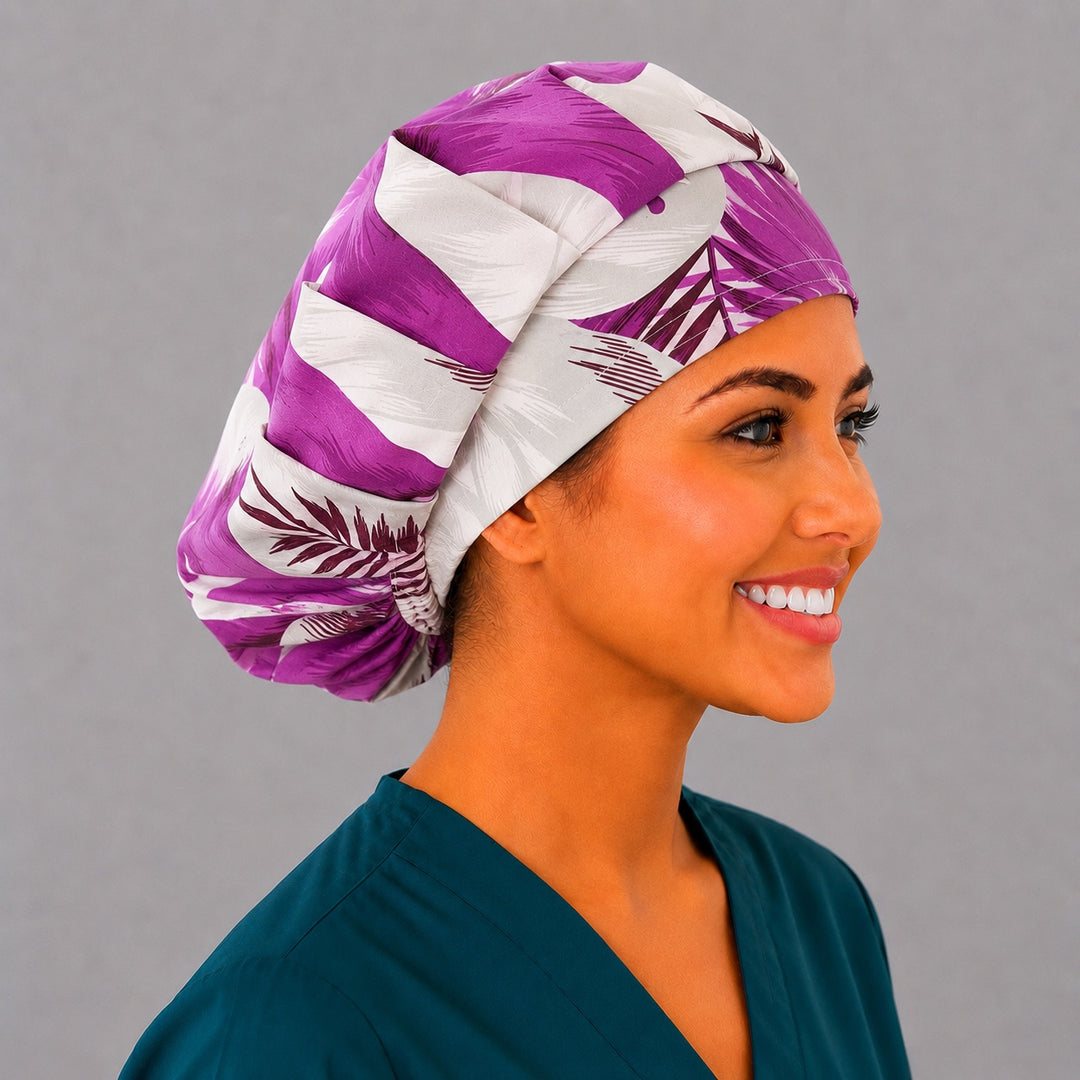 Purple tropical floral bouffant scrub cap left three-quarter angle on smiling model showing violet and plum hibiscus blooms with palm fronds on cream, women&