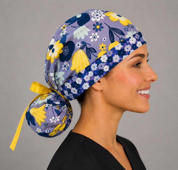 Purple and yellow floral ponytail scrub cap back view close-up showing gathered pouch full of lavender and yellow summer flowers and yellow ribbon bow