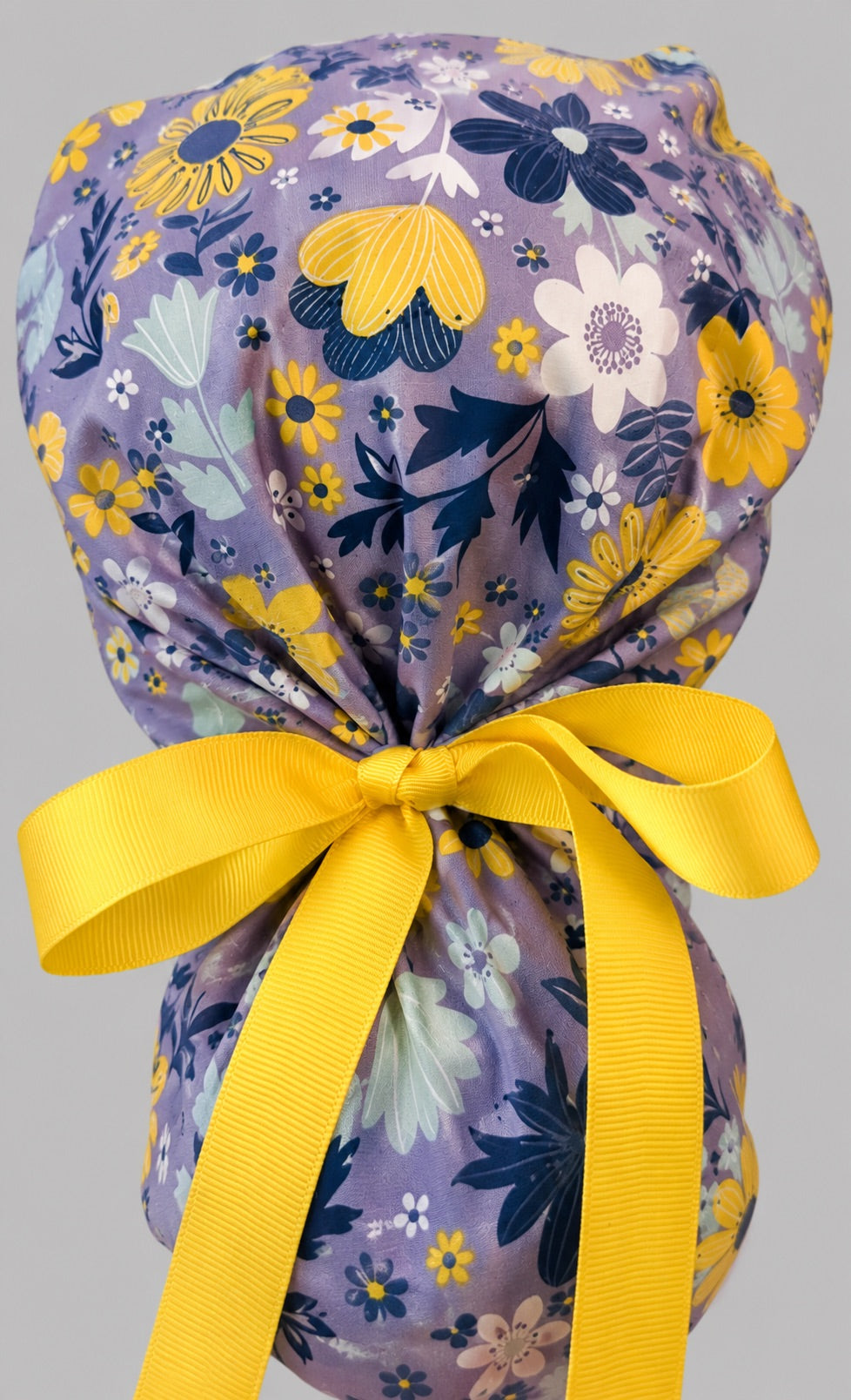 Purple and yellow floral ponytail scrub cap right side profile showing gathered pouch of summer wildflowers on lavender and long yellow ribbon ties
