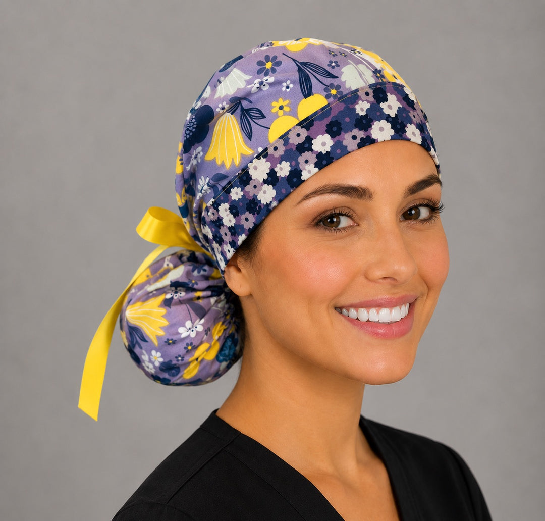 Purple and yellow floral ponytail nurse cap right three-quarter angle on smiling model showing lavender and yellow summer flowers and yellow ribbon bow