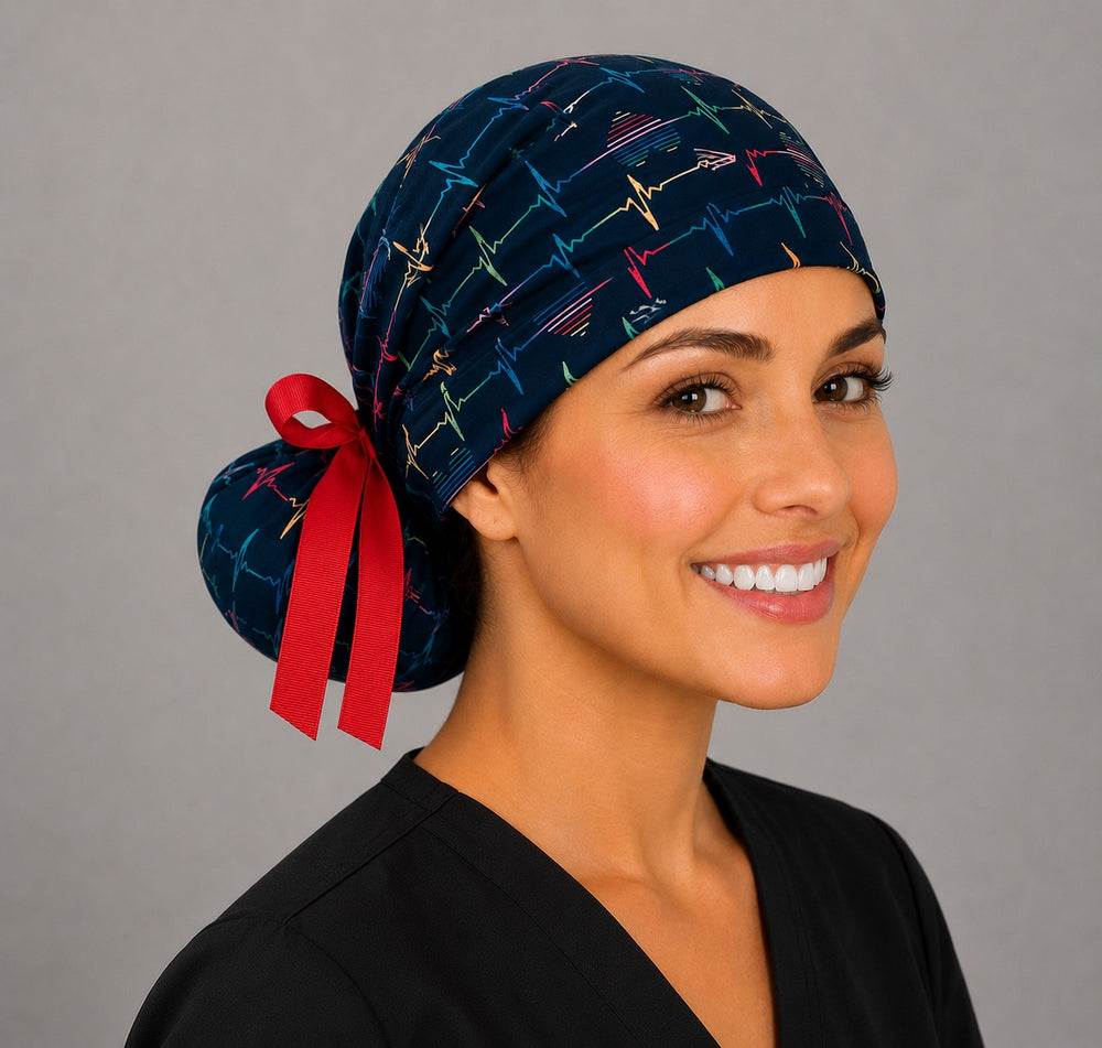 Rainbow EKG heartbeat ponytail nurse cap left three-quarter angle on smiling model showing colorful heartbeat lines, hearts on navy and red grosgrain ribbon bow