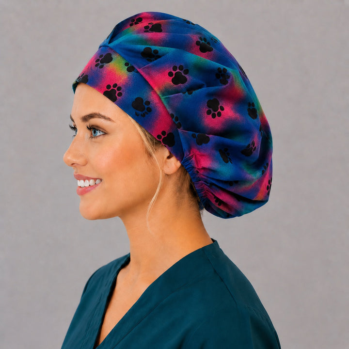 Left side profile of the rainbow paw print bouffant surgical hat — magenta and teal watercolor wash, roomy breathable cotton cap for nurses