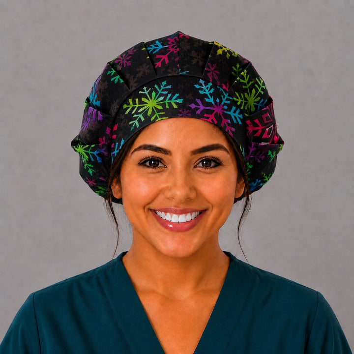 Woman wearing a rainbow snowflake bouffant scrub cap, front view — colorful snowflakes on textured black, adjustable women&