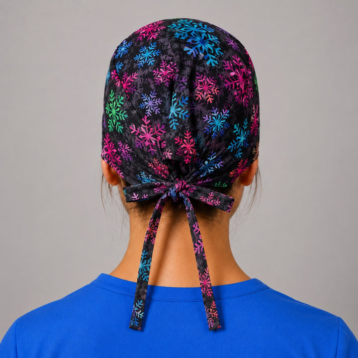 Rainbow snowflake scrub cap for short hair, handmade black tie-back winter surgical hat on OR nurse, front view