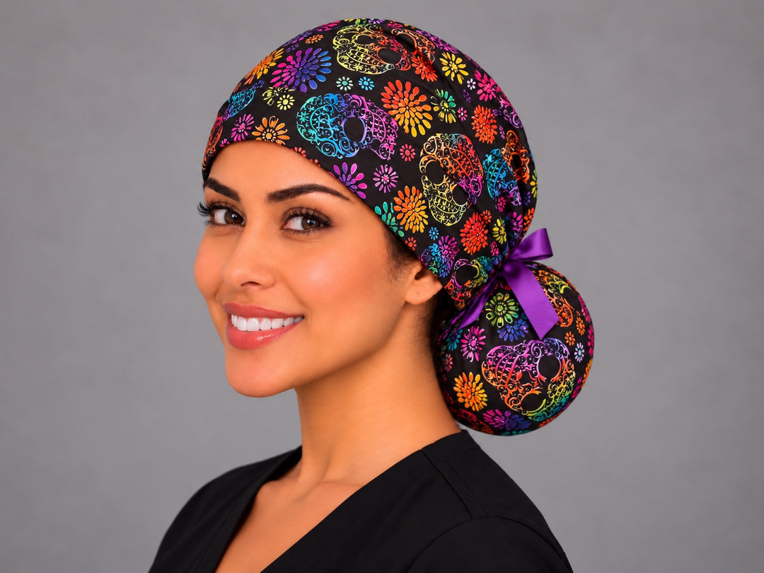 Rainbow sugar skull ponytail scrub cap, left three-quarter view, Mexican Día de los Muertos surgical hat for long hair with purple bow