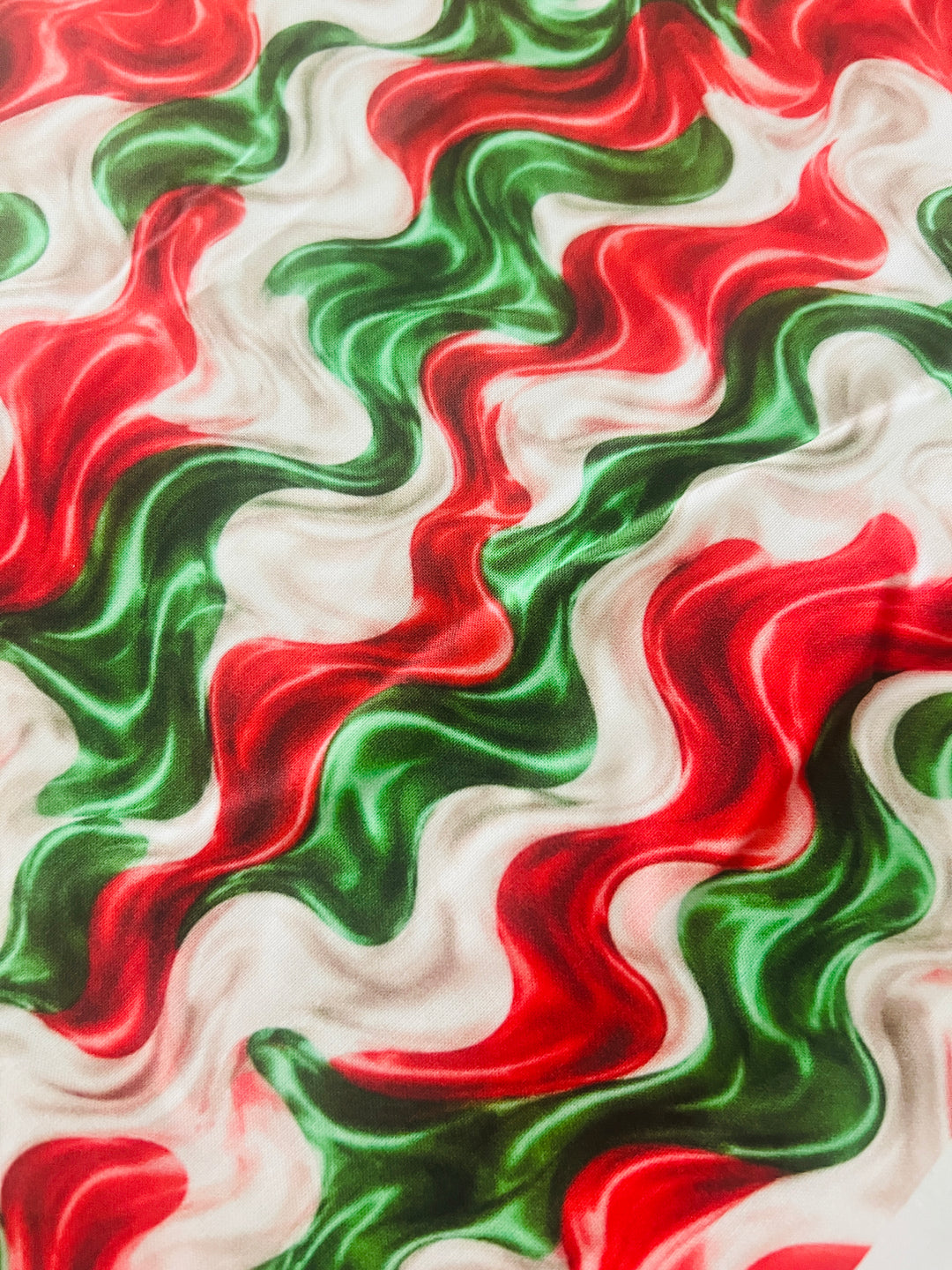 Close-up of the red, green and cream marble swirl cotton fabric, showing the glossy painted texture of the wavy print