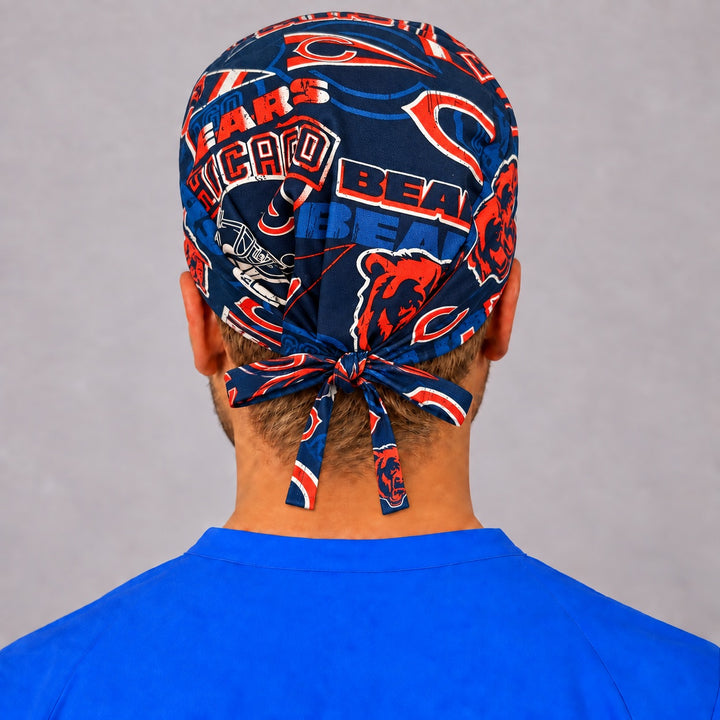 Right three-quarter view of a retro navy and orange football surgical hat for men, showing distressed helmet and pennant graphics across the side panel and a short tied bow