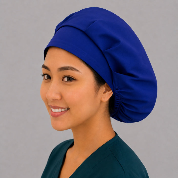 Royal blue bouffant scrub cap left three-quarter angle on smiling model showing solid royal blue fabric and thick front band, OR World nurse hat