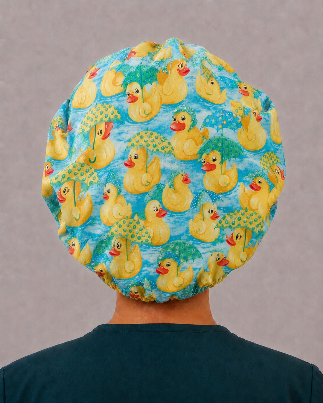 Back view of the rubber duckie bouffant scrub cap — full gathered fit showing ducks and polka-dot umbrellas across the aqua crown