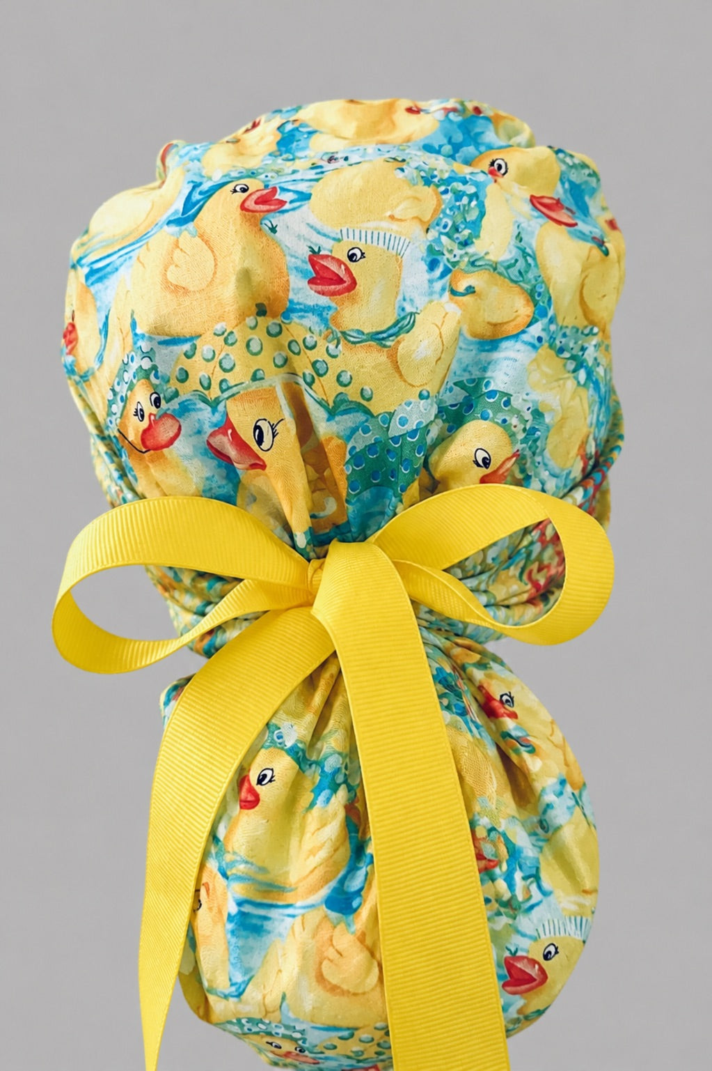 Rubber duckies rain boots ponytail scrub cap back view close-up showing gathered pouch full of yellow rubber ducks on aqua water with yellow ribbon bow