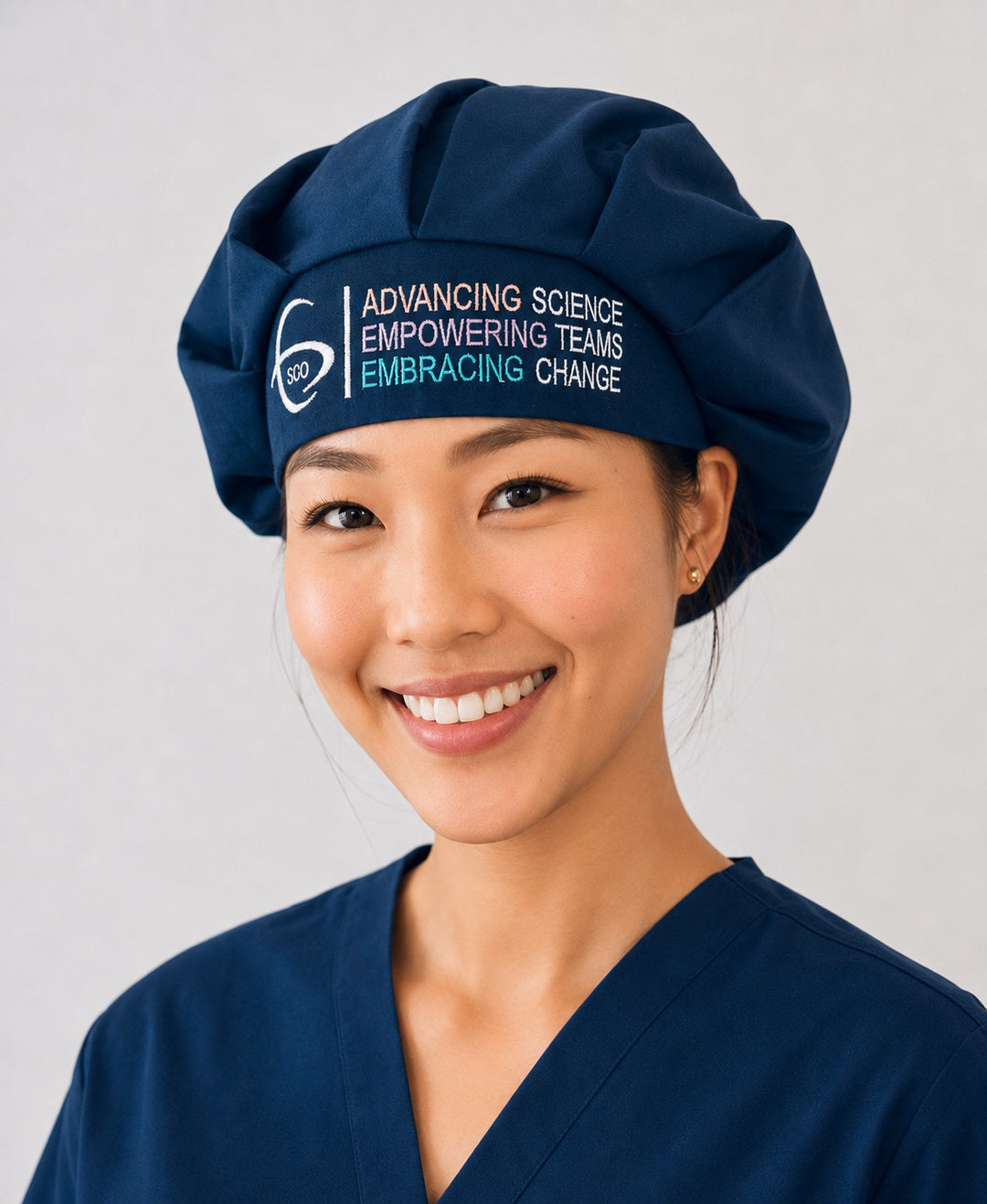 Close-up of the official SGO logo embroidery, Advancing Science Empowering Teams Embracing Change, on a navy bouffant scrub cap