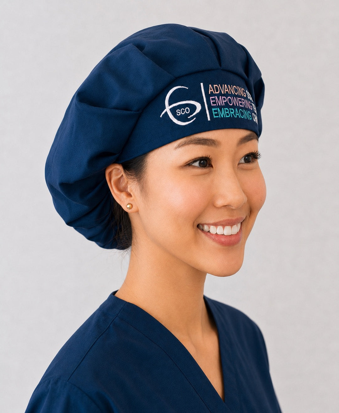 Three-quarter view of a healthcare professional wearing the navy SGO official embroidered bouffant surgical scrub cap showing the roomy bouffant crown and logo