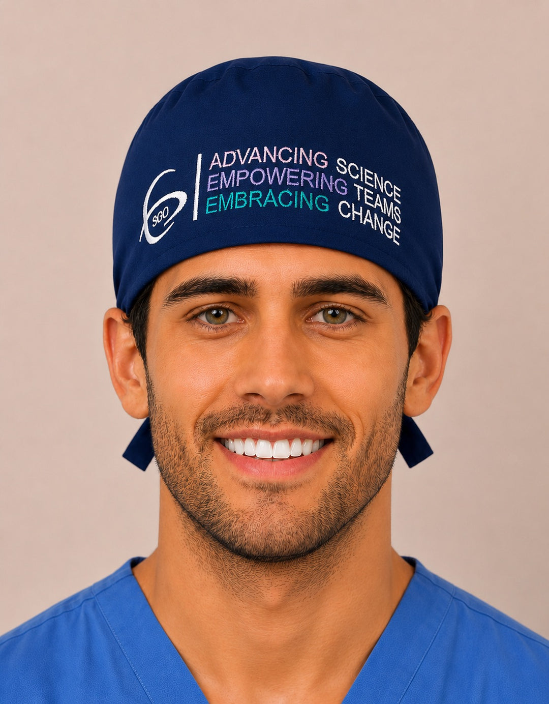 Smiling male surgeon in a navy SGO official embroidered traditional tie-back surgical scrub cap with the full-color Society of Gynecologic Oncology logo