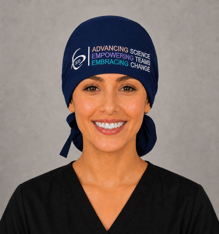 Smiling OR nurse wearing a navy SGO official ponytail surgical scrub cap with the full-color Society of Gynecologic Oncology logo and Advancing Science Empowering Teams Embracing Change tagline across the front band