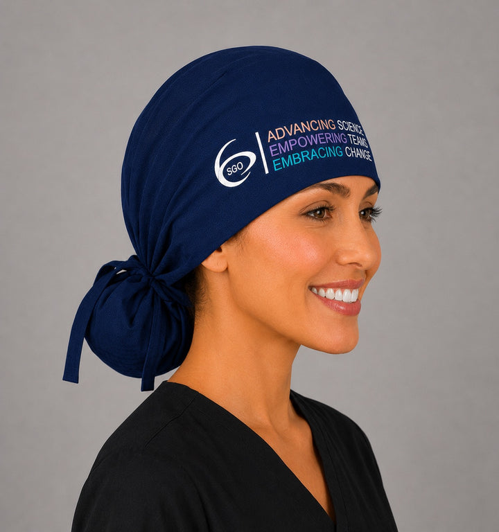 Side profile of the navy SGO official ponytail scrub cap showing the tie-back gathered hair pouch for long thick hair and the embroidered Society of Gynecologic Oncology logo