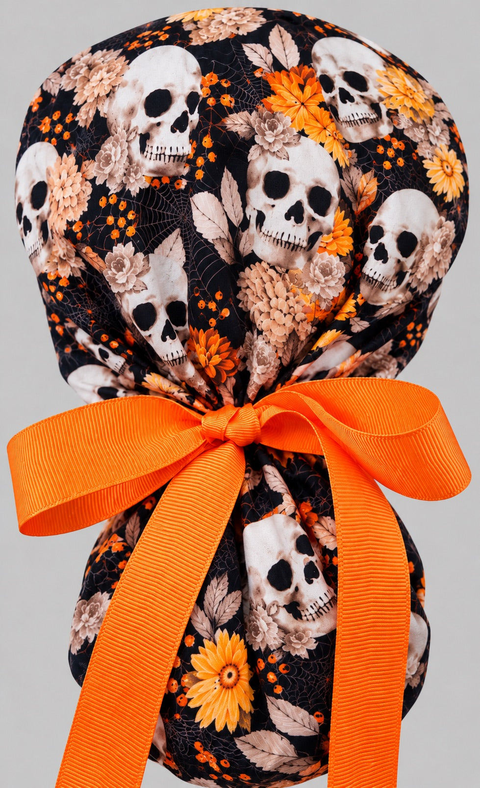 Back view of the skulls and flowers ponytail cap, showing the gathered crown and long orange grosgrain ribbon tails tied in a wide bow