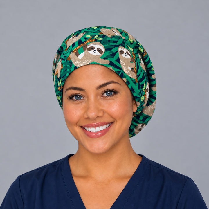 Woman wearing a cute sloth Euro scrub cap, front view — hanging sloths in green jungle leaves, adjustable surgical hat for nurses