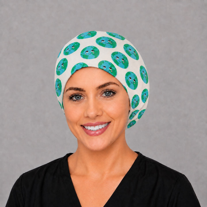 Woman wearing a smiling earth Euro scrub cap, front view — kawaii green globe faces on white, adjustable cotton surgical hat for women