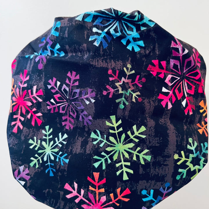 Side view of rainbow snowflake bouffant scrub cap — handmade USA Christmas winter surgical hat for OR nurses with long hair.