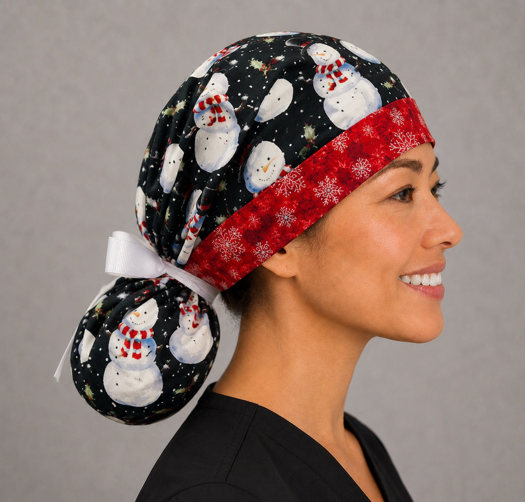 Snowmen ponytail nurse cap right three-quarter angle on smiling model showing snowmen in striped hats on black with red snowflake band and white ribbon bow