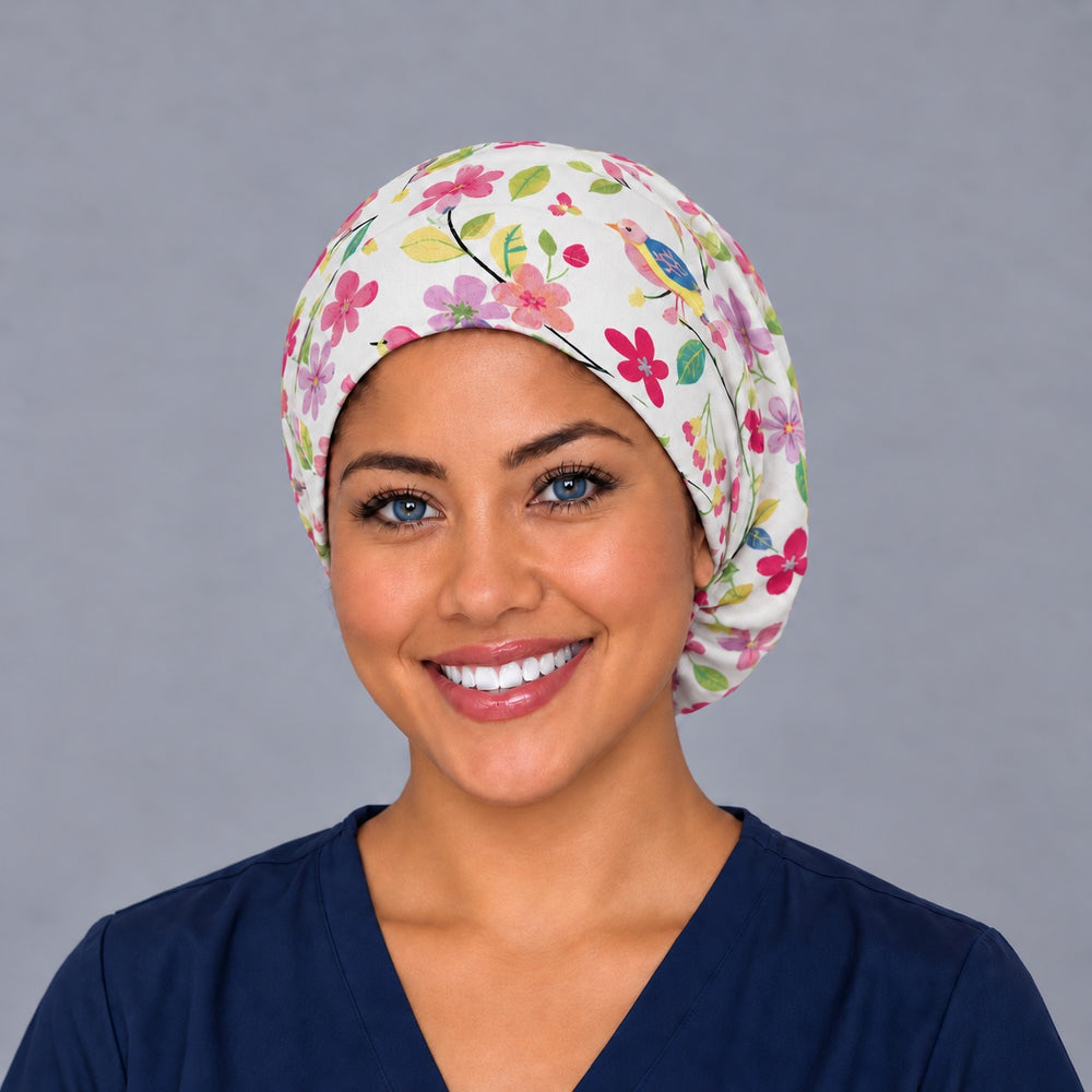Woman wearing a spring birds and flowers Euro scrub cap, front view — folk-art songbirds and blossoms on white, adjustable surgical hat