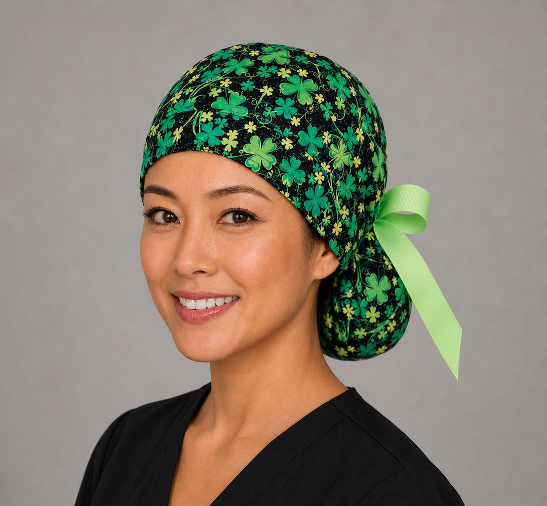 St. Patrick's glitter clovers ponytail scrub cap right three-quarter angle on smiling model showing green four-leaf clovers and glitter on black with lime green ribbon bow