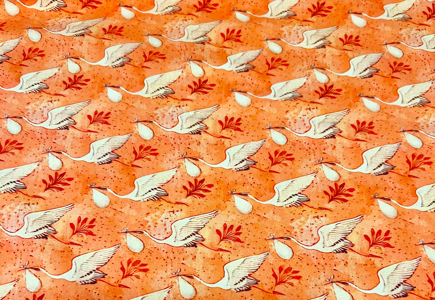 Close-up of coral stork and crane fabric print for L&D ponytail scrub cap, white storks carrying baby bundles, OR World