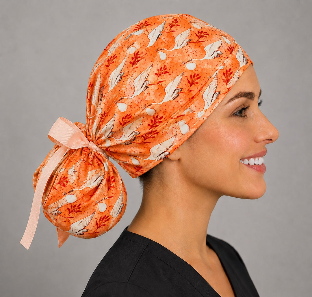 Profile view of coral stork ponytail scrub cap with peach ribbon ties for women with long hair, labor and delivery surgical hat, handmade USA, OR World