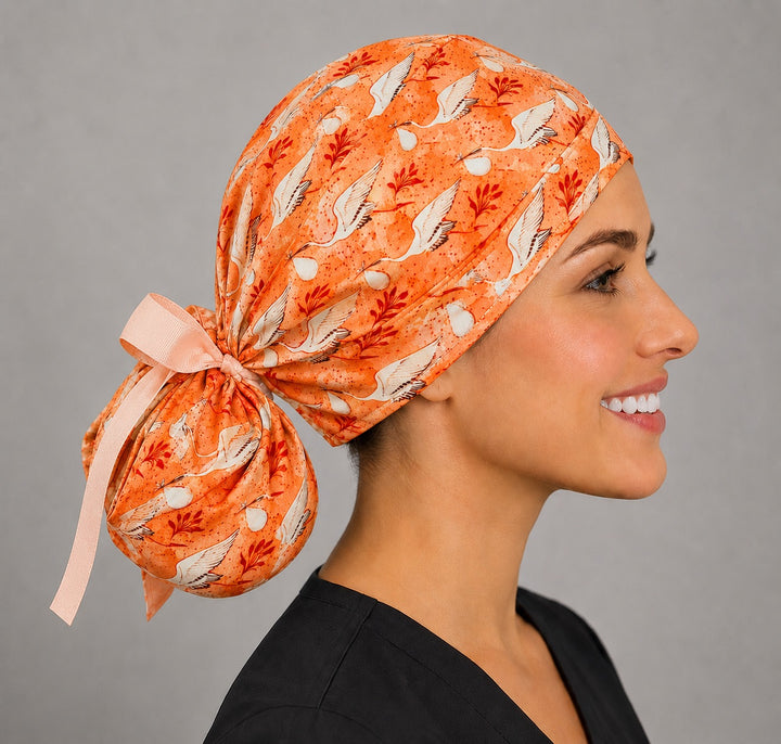 Profile view of coral stork ponytail scrub cap with peach ribbon ties for women with long hair, labor and delivery surgical hat, handmade USA, OR World