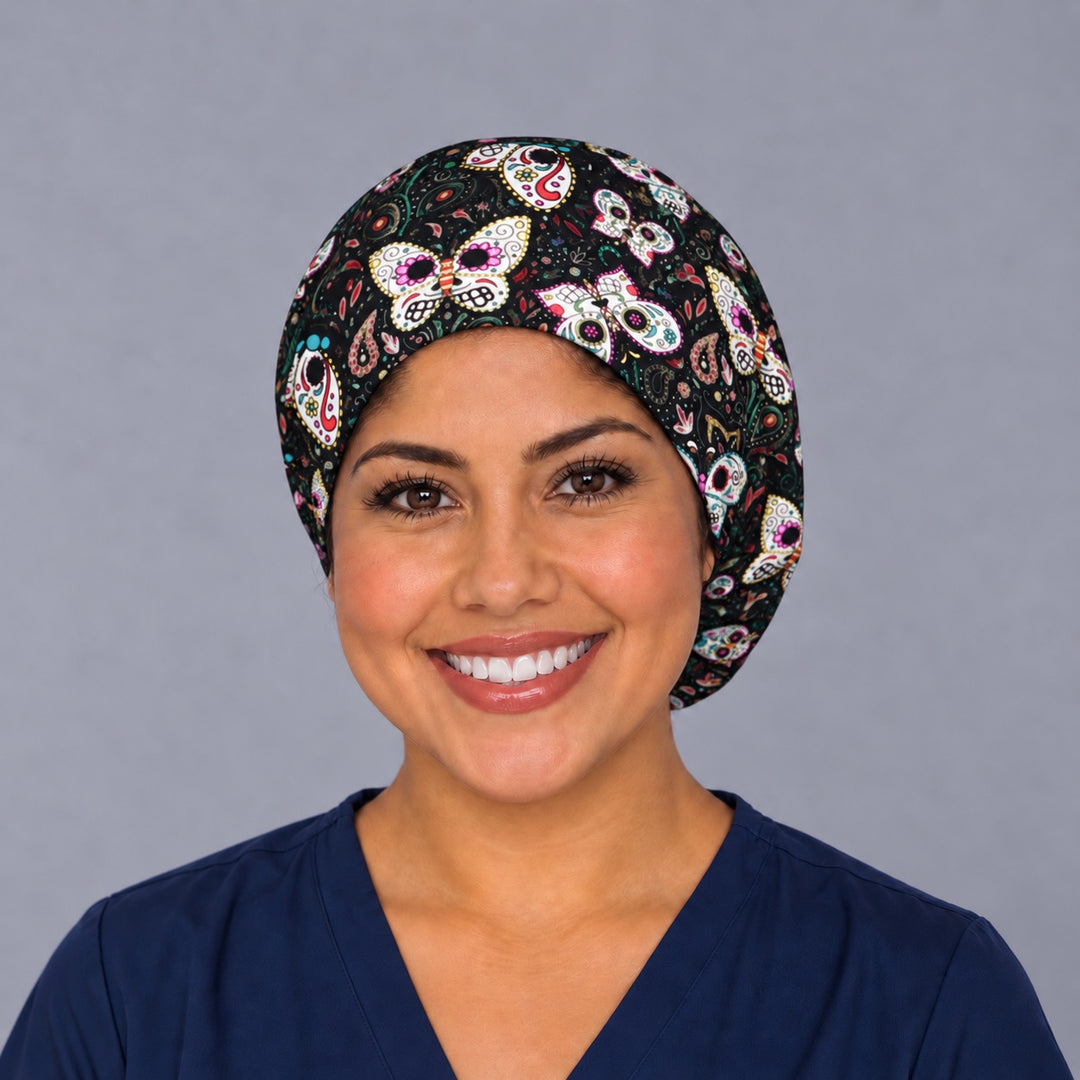 Woman wearing a sugar skull butterfly Euro scrub cap, front smiling view — Día de los Muertos butterflies on black, adjustable surgical hat