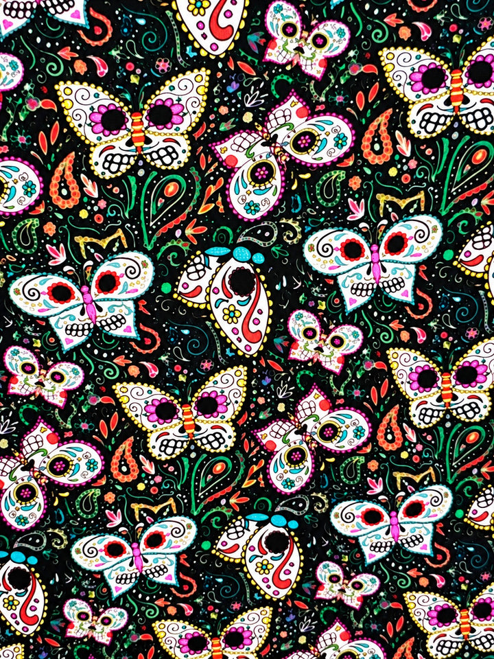 Fabric close-up for the sugar skull butterfly ponytail cap, skull winged mariposas with coral paisley and green vines on black premium cotton