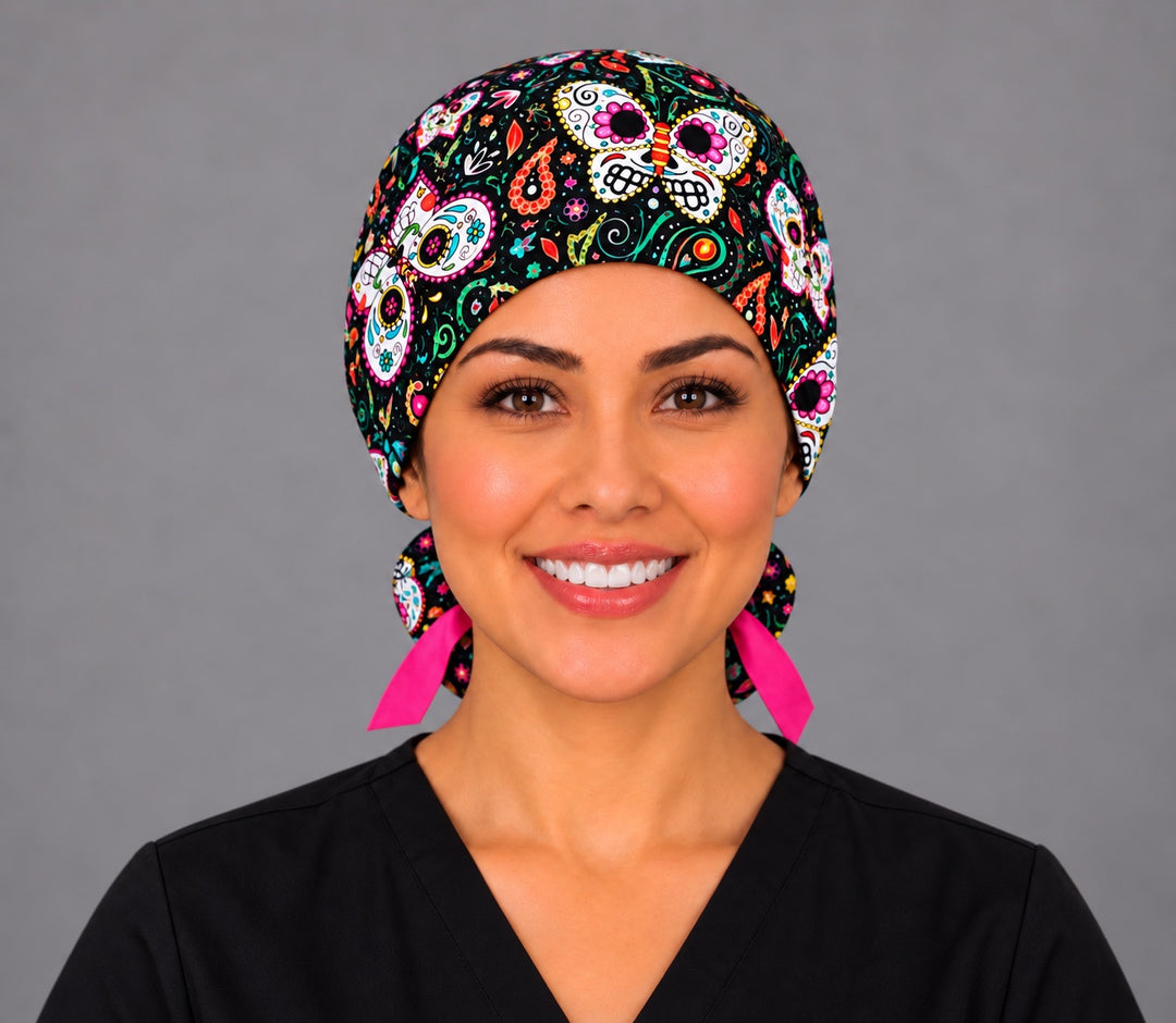 Front view of a nurse in the black sugar skull butterfly ponytail scrub cap, calavera butterflies across the band and hot pink ribbon ties at the neck