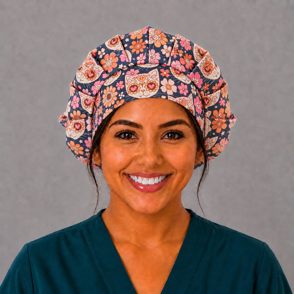 Woman wearing a Fiesta Gato sugar skull cat bouffant scrub cap, front view — calavera cat faces and coral flowers on navy, adjustable women's surgical hat