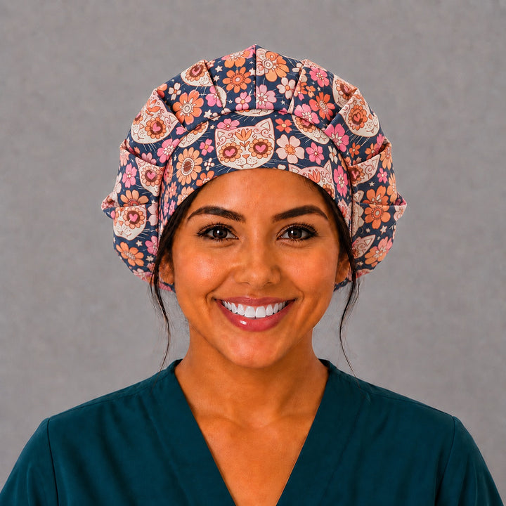 Woman wearing a Fiesta Gato sugar skull cat bouffant scrub cap, front view — calavera cat faces and coral flowers on navy, adjustable women&