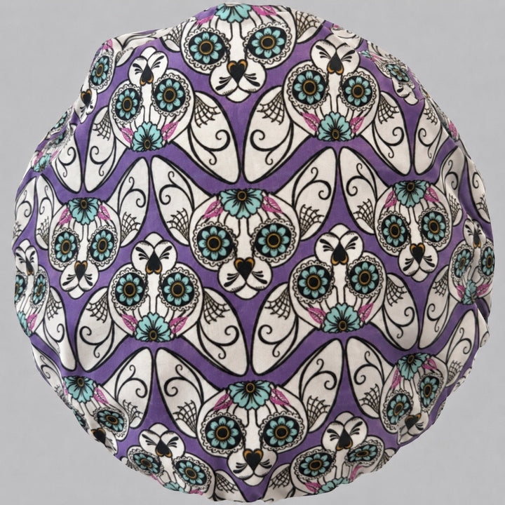 Top view of the sugar skull cat bouffant scrub cap — full purple crown showing the mirrored calavera cat pattern