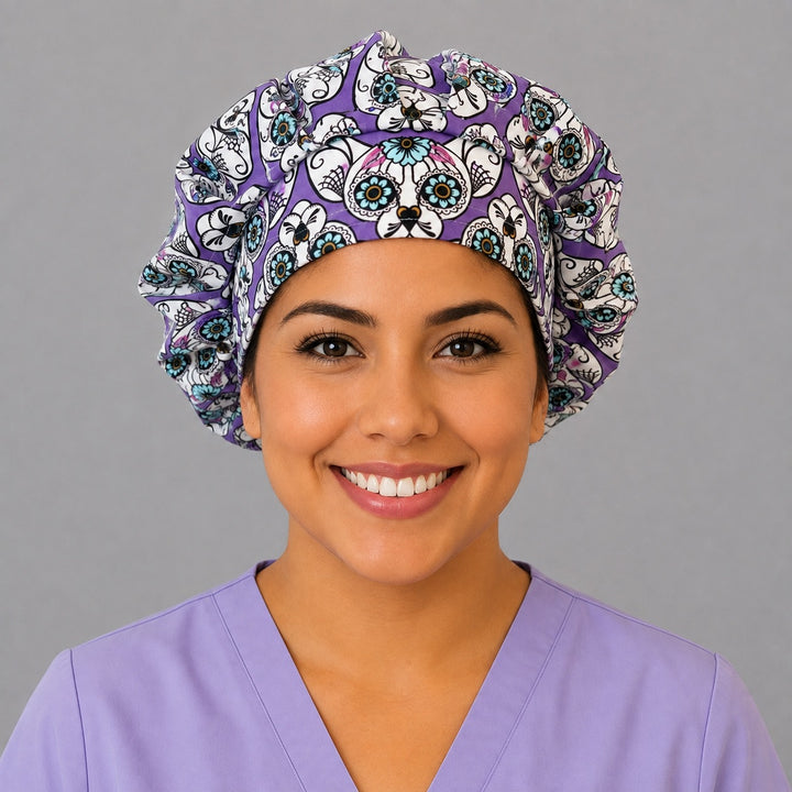 Woman wearing a purple sugar skull cat bouffant scrub cap, front view — calavera cat faces with teal flower eyes on violet, adjustable women&
