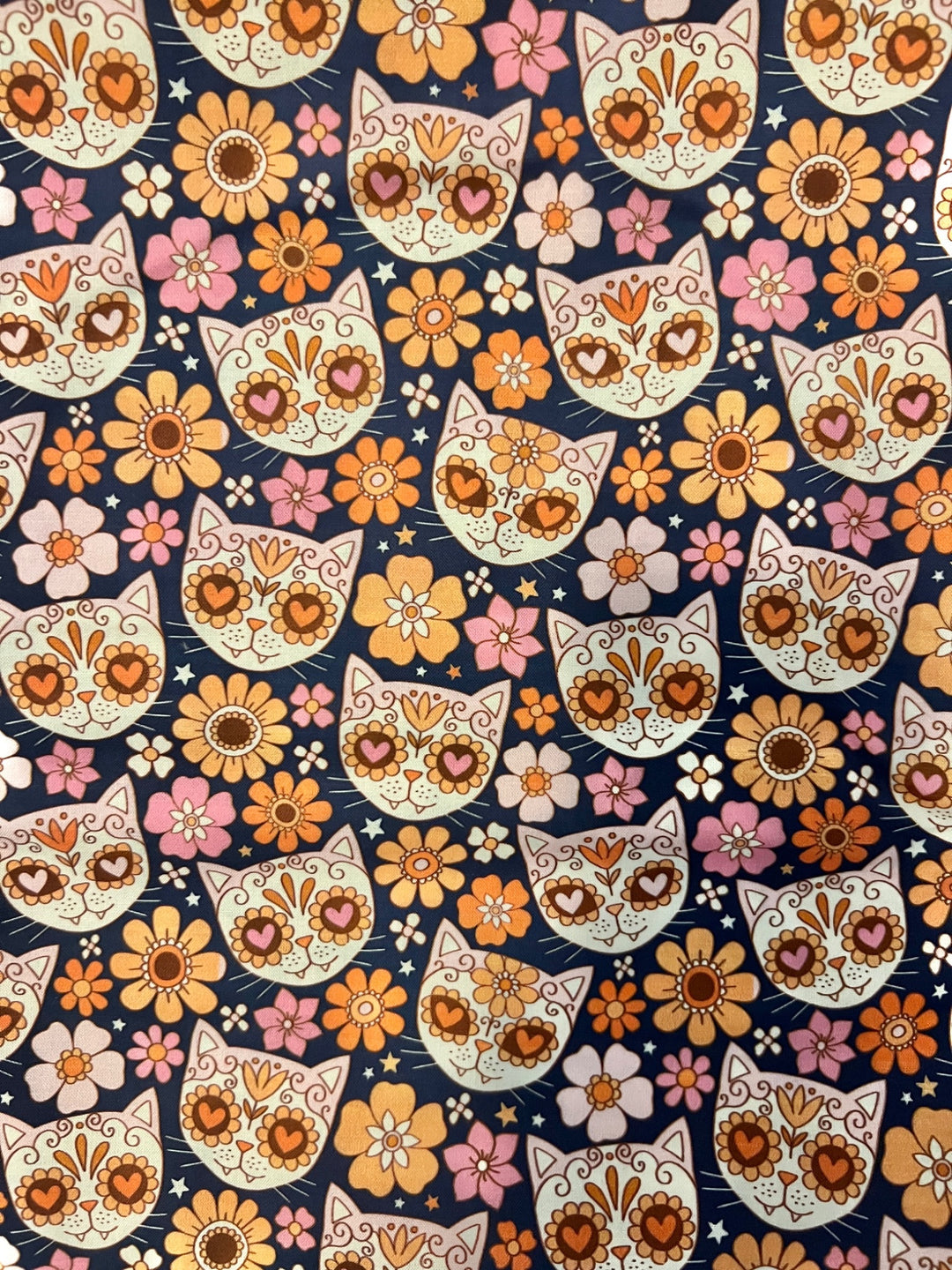 Fabric close-up for the sugar skull cat ponytail cap, heart-eyed calavera kitties with marigold, peach and pink flowers on navy premium cotton