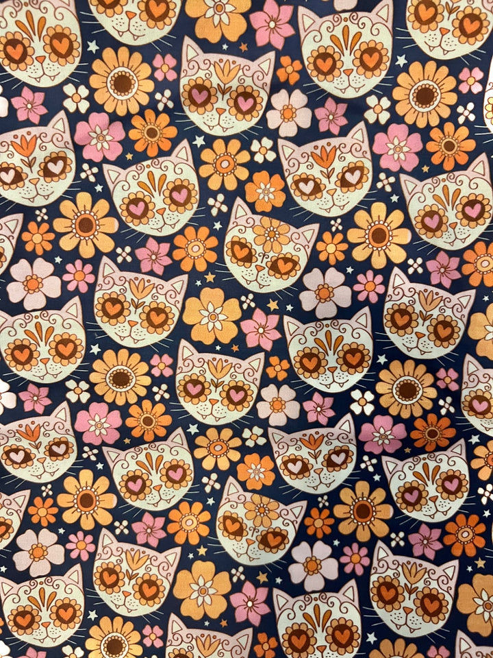 Fabric close-up for the sugar skull cat ponytail cap, heart-eyed calavera kitties with marigold, peach and pink flowers on navy premium cotton