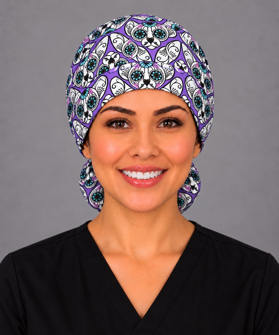 Woman wearing a purple sugar skull cat ponytail scrub cap, front view — calavera cats with teal flower eyes, Mexican surgical hat for long hair