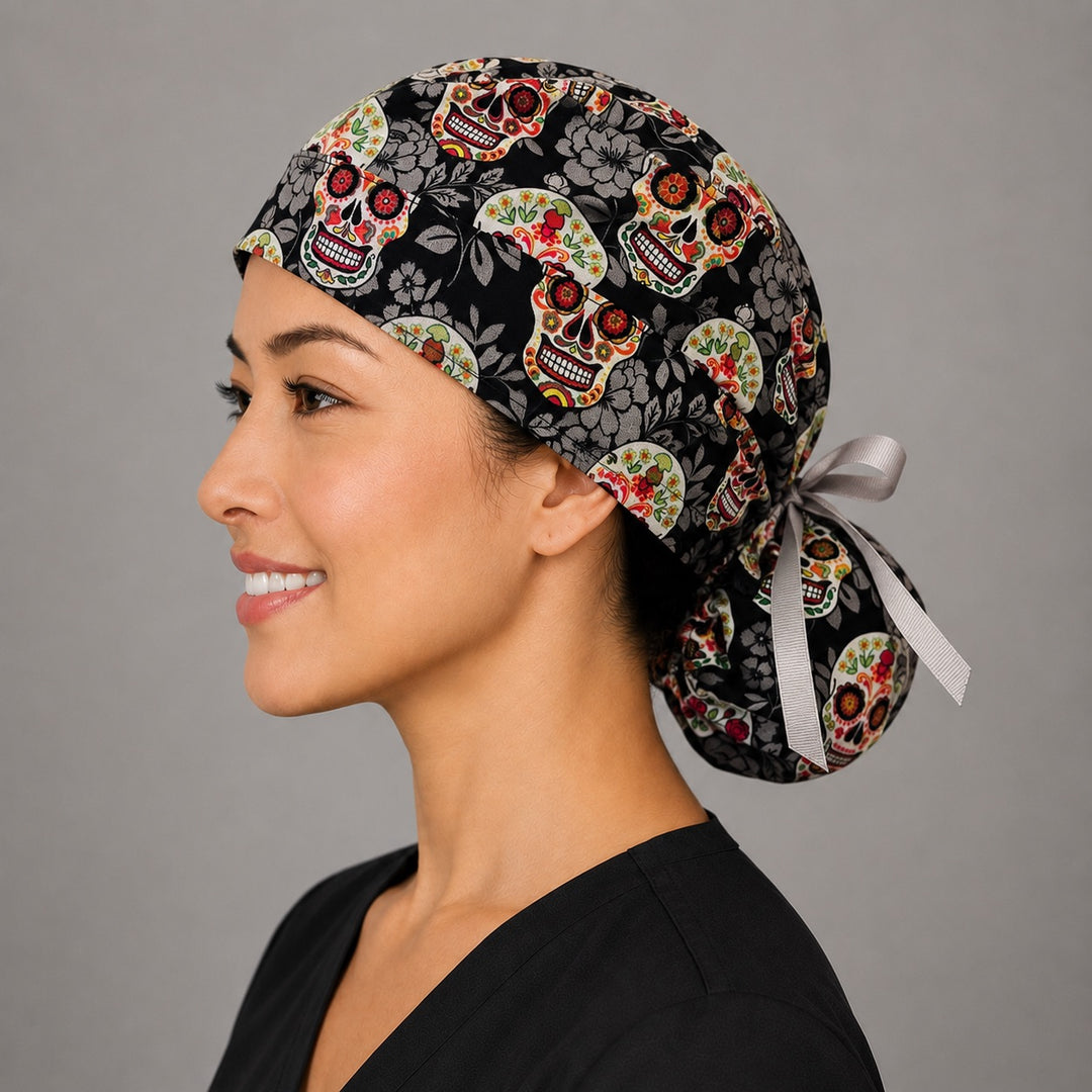 Sugar skull Halloween ponytail nurse cap front angle on smiling model showing Day of the Dead skulls on black floral print with gray ribbon bow