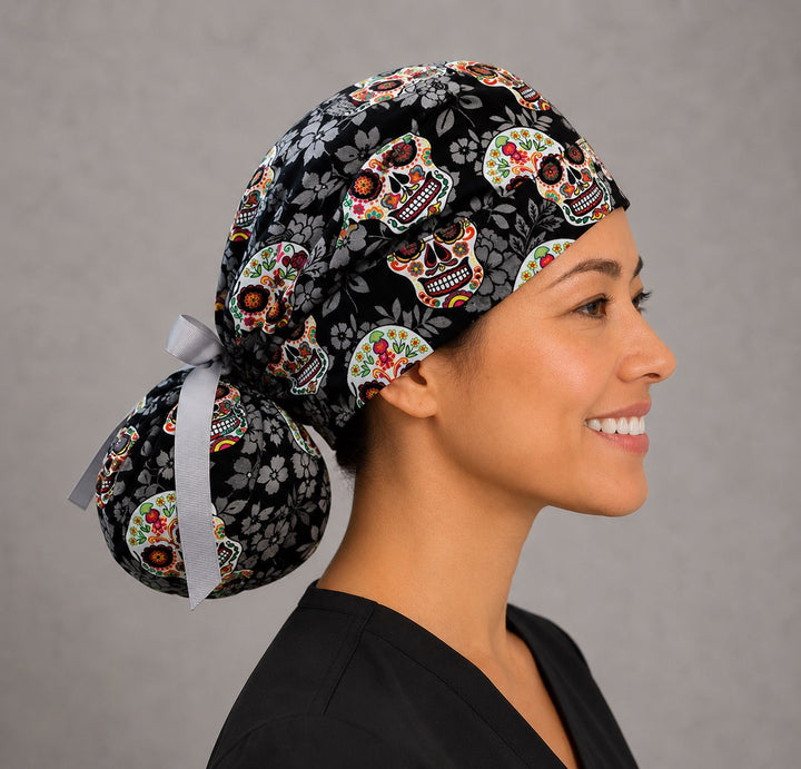 Sugar skull Halloween ponytail scrub cap right three-quarter angle showing gathered ponytail pouch of Day of the Dead skulls on black floral print with gray ribbon bow